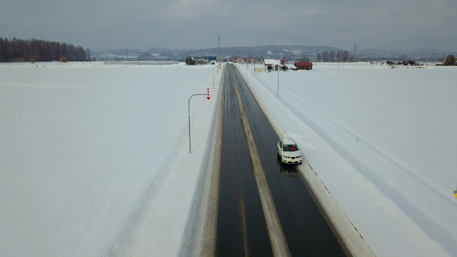 航拍汽车行驶在日本北海道冬季雪原乡村公路