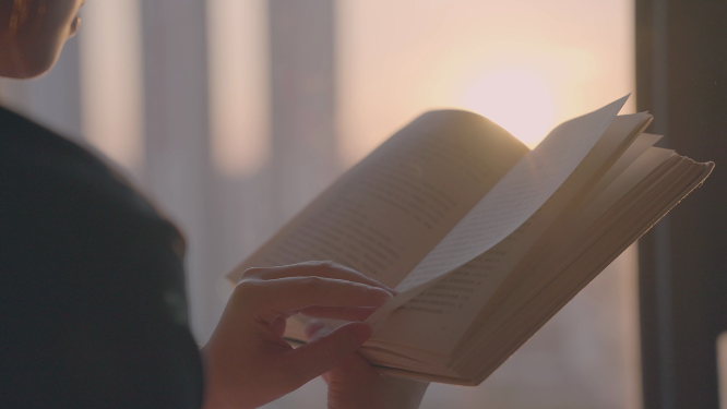 女孩在夕阳下的落地窗边看书翻书4k视频